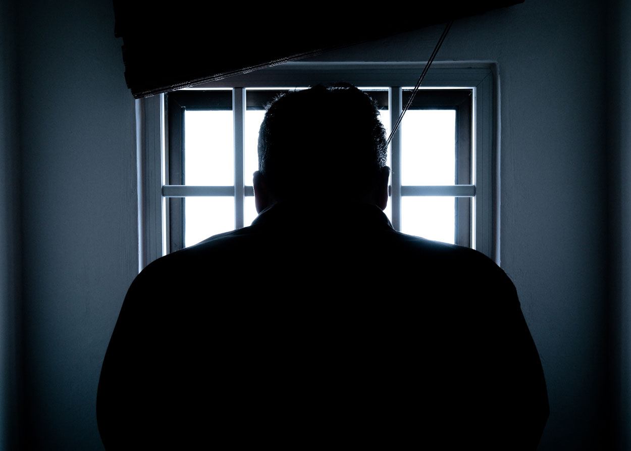man's silhouette standing in front of a jailhouse window